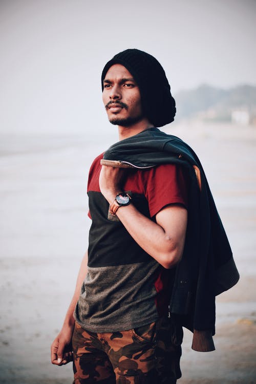 男子手持黑色服装站在水的附近 · 免费素材图片