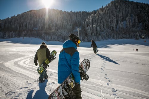 在晴朗的天空下穿蓝色冬季夹克携带滑雪板的人 · 免费素材图片