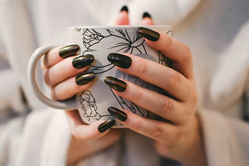 拿着白色和灰色的花卉陶瓷杯的黑指甲的女人 · 免费素材图片