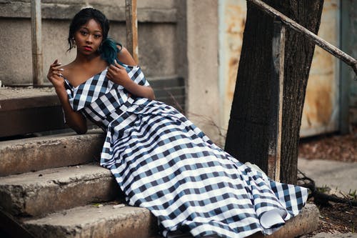女人穿着黑色和白色格仔的意粉表带冷肩连衣裙坐在楼梯上 · 免费素材图片