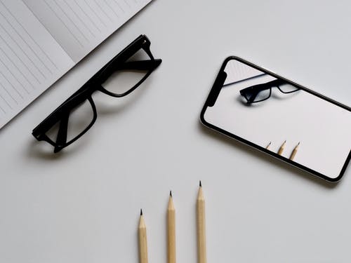 三支铅笔，眼镜和白表上的智能手机 · 免费素材图片