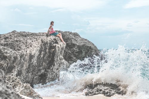 女人坐在岩石附近的水体 · 免费素材图片