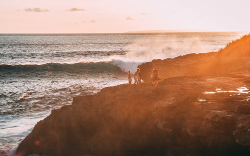站在悬崖上的人们在水体黄金时段摄影附近 · 免费素材图片