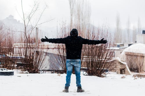 人穿着黑色外套和蓝色牛仔牛仔裤，站在积雪覆盖的田野上 · 免费素材图片