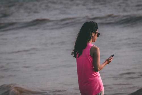 女人穿着粉红色背心站在海边 · 免费素材图片