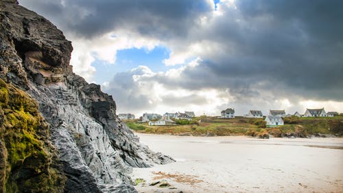 灰色岩石峭壁旁边的白色沙滩 · 免费素材图片