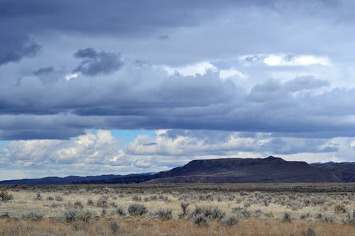 灰色的草田，导致灰色大云下的山脉 · 免费素材图片