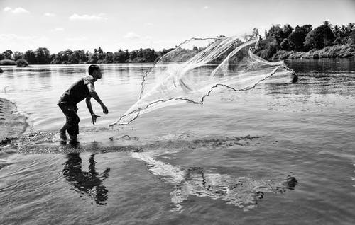 男子投掷渔网的灰度照片 · 免费素材图片