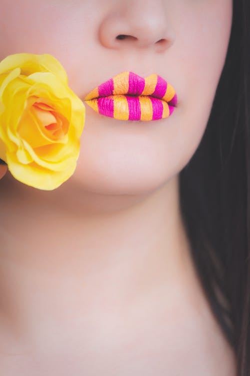 女人穿着黄色和粉红色的条纹的唇膏，拿着黄色的玫瑰 · 免费素材图片