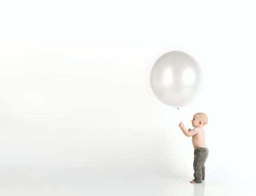 站立时拿着白色气球的黑裤子的婴儿 · 免费素材图片