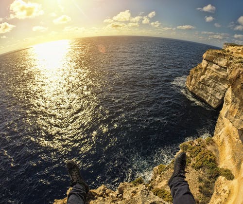 日落期间，在海边的石岛顶上的人 · 免费素材图片