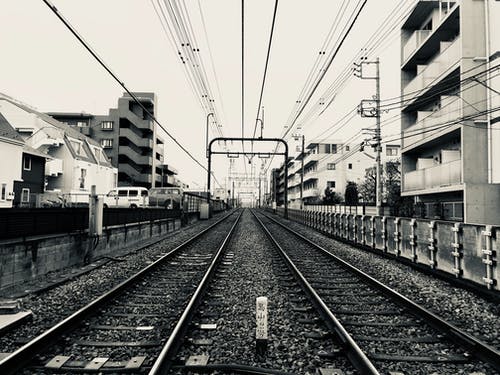 建筑物之间的火车轨道的灰度摄影 · 免费素材图片