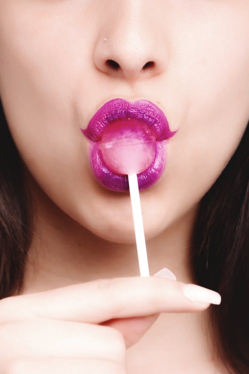 女人穿着紫色唇膏与粉红色的棒棒糖 · 免费素材图片