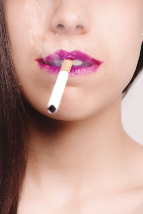 棕色头发的女人，用粉红色的口红咬白香烟棒 · 免费素材图片