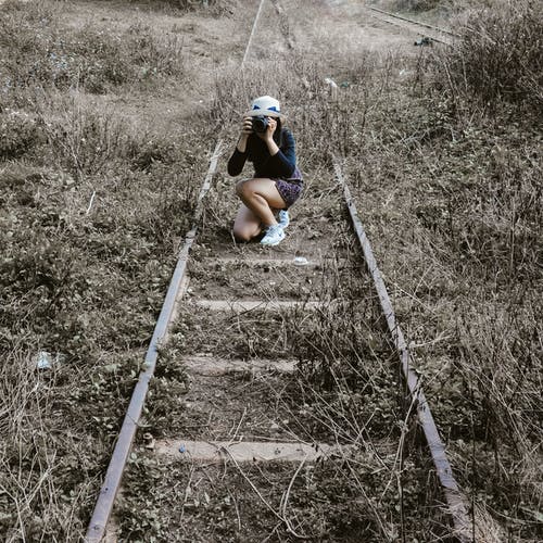 女人白色圆帽在铁路路上拿着黑色的单反相机 · 免费素材图片