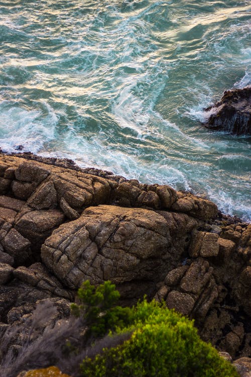 白天绿色水体旁边的棕色岩层 · 免费素材图片
