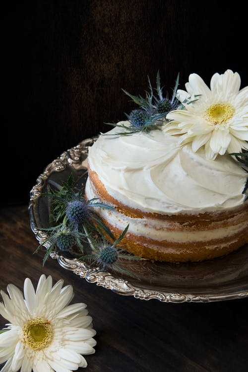 翻糖蛋糕打成白色的糖霜，上面放着灰色不锈钢板上的白色花瓣花 · 免费素材图片