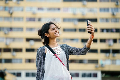 微笑的女士拿着黑色的智能手机 · 免费素材图片