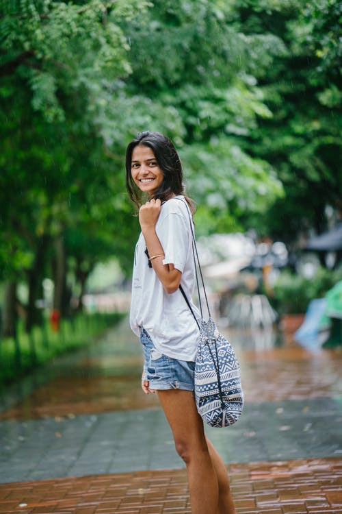 浅焦点女人穿着白衬衫和蓝色牛仔短裤在绿树附近的街道上的摄影 · 免费素材图片