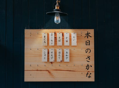 汉字印刷的标签挂在吊灯照亮的棕色木板上 · 免费素材图片