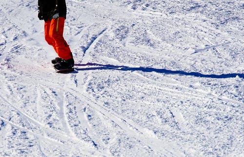 穿着黑色上衣和橙色裤子骑单板滑雪的人的照片 · 免费素材图片