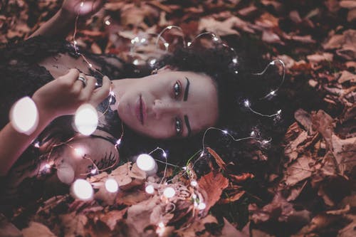 女人躺在干树叶，拿着串灯 · 免费素材图片