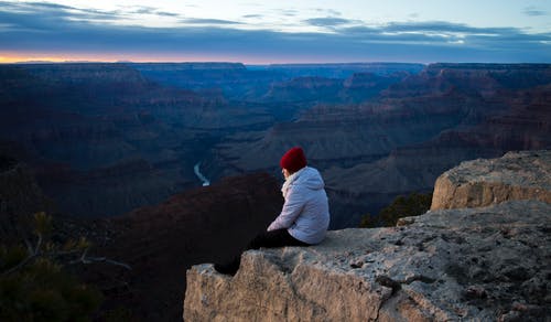 白天坐在悬崖上的人穿白色连帽衫 · 免费素材图片
