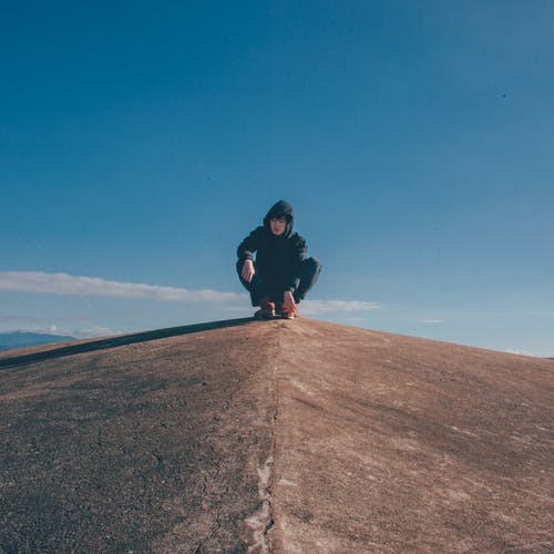 黑色连帽衫和裤子坐在岩石峭壁上的男人 · 免费素材图片