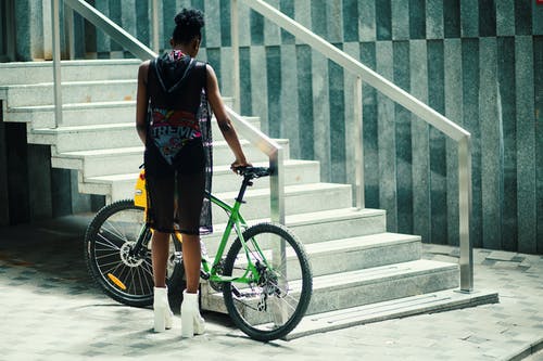 在金属楼梯附近拿着绿色的山地自行车的黑色无袖衬衫的男人 · 免费素材图片