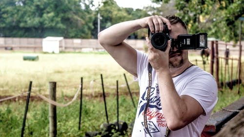 男子拿着单反相机站在栅栏附近 · 免费素材图片