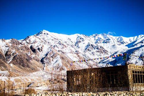 晴朗的蓝天下，白雪覆盖的山脉底部的石材建筑 · 免费素材图片