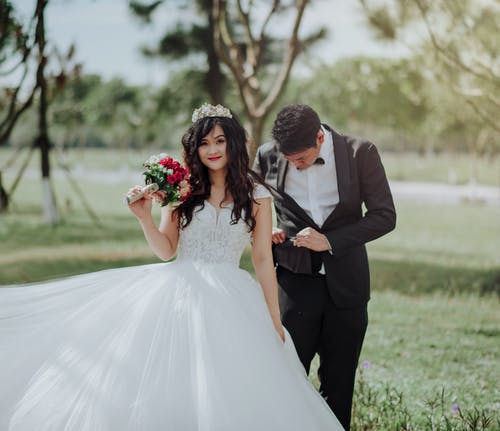 穿着婚纱的男人，拿着花与男人在黑色西装外套的女人 · 免费素材图片