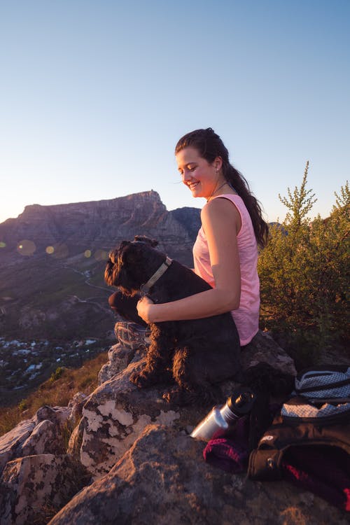 女人穿着粉红色背心坐在狗旁边的岩石上 · 免费素材图片