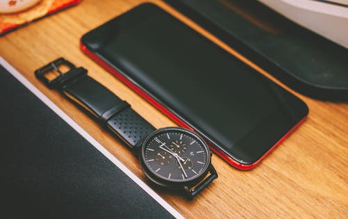 在棕色木板黑色计时表旁边的红色智能手机 · 免费素材图片