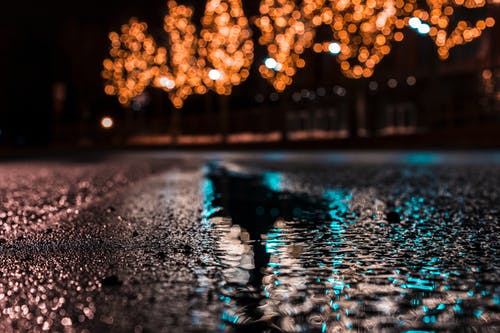 夜间在城市灯光下有水滴的沥青路面的选择性聚焦摄影 · 免费素材图片