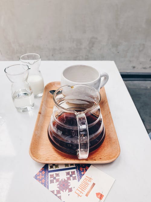 棕色玻璃托盘上的白色杯子附近的透明玻璃咖啡壶 · 免费素材图片
