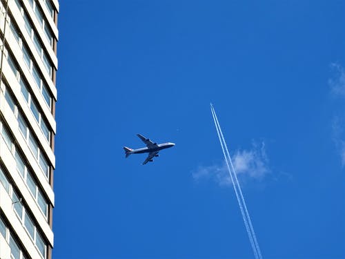 白色混凝土建筑物和白色轨迹附近空中的白色飞机低角度摄影 · 免费素材图片