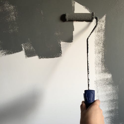 在粉刷墙壁时拿着油漆滚筒的人 · 免费素材图片