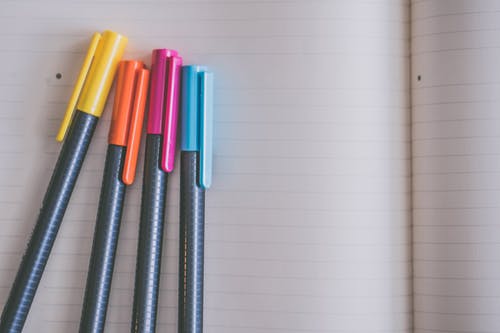 白色笔记本上的黄色，橙色，粉色和蓝色着色笔 · 免费素材图片