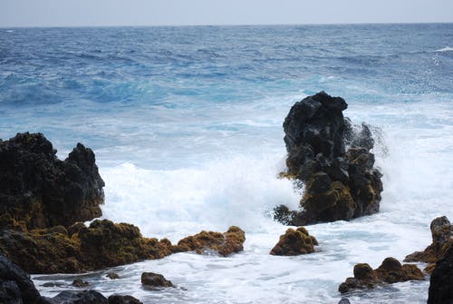 白天在蓝天下被水体包围的大石头 · 免费素材图片