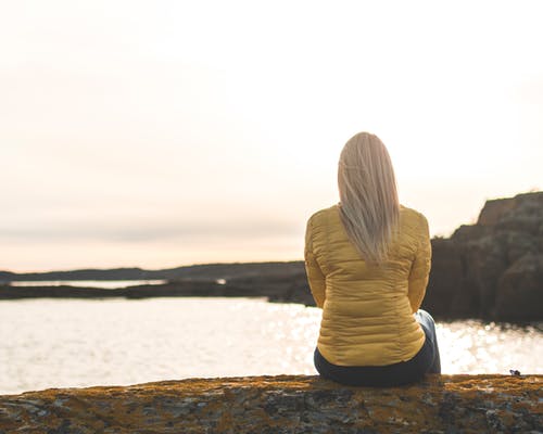 女人穿着黄色泡泡夹克坐在海前 · 免费素材图片