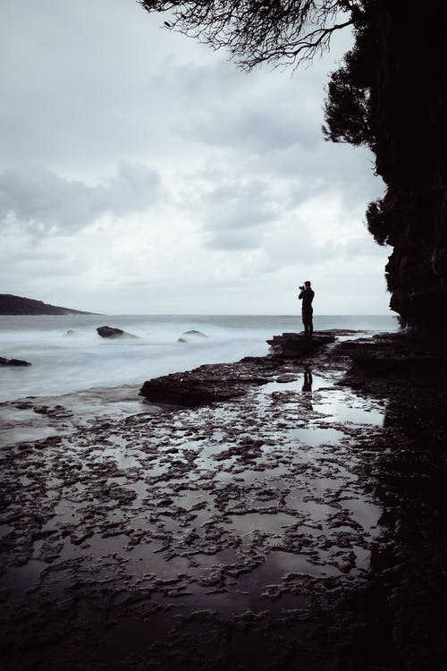 站在海洋附近的岩石上的人 · 免费素材图片