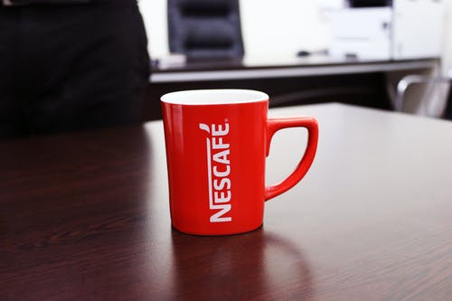 棕色的木桌上的红色和白色雀巢咖啡杯子 · 免费素材图片