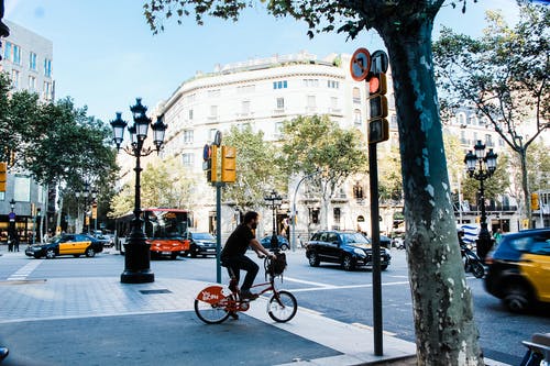 男人在大街上穿蓝色t恤骑自行车 · 免费素材图片