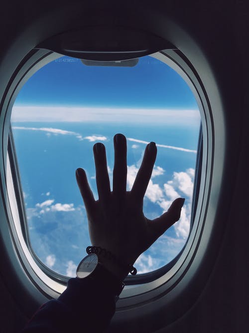 人的左手触摸飞机窗口的摄影 · 免费素材图片