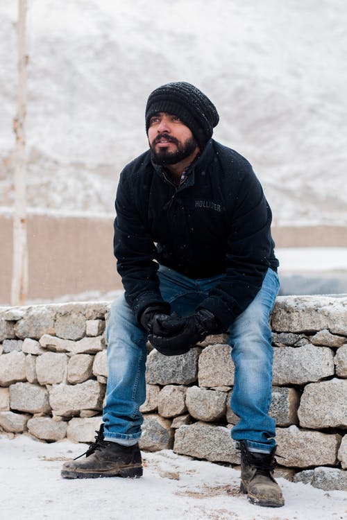 男子坐在岩石上，穿着黑色外套 · 免费素材图片