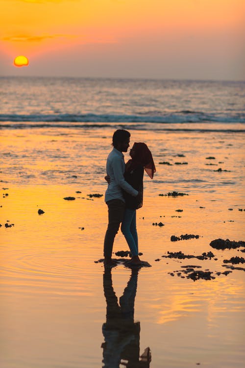 男人和女人在日落期间在海边拥抱 · 免费素材图片