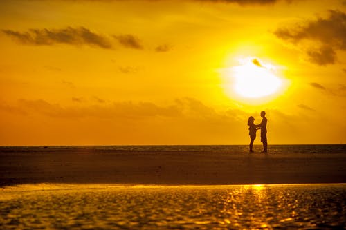 男人和女人站在海边日落下 · 免费素材图片