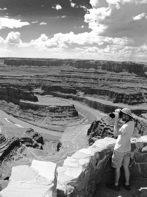 男子站在大峡谷灰度照片附近拿着相机 · 免费素材图片