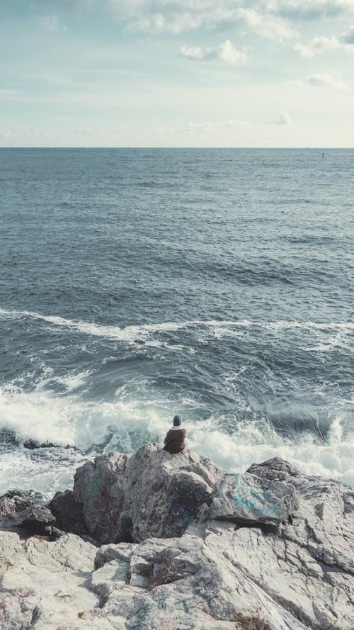 坐在海边的灰色岩石上的人 · 免费素材图片